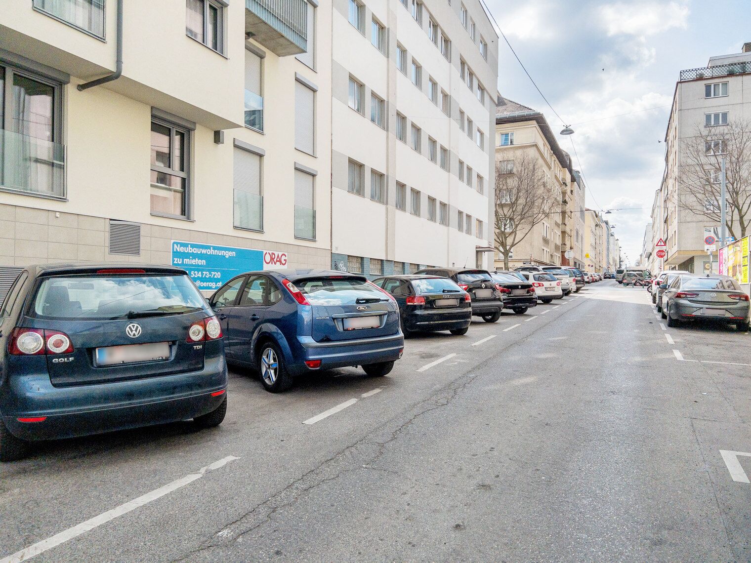 Una hilera de coches aparcados a lo largo de una calle urbana flanqueada por edificios.