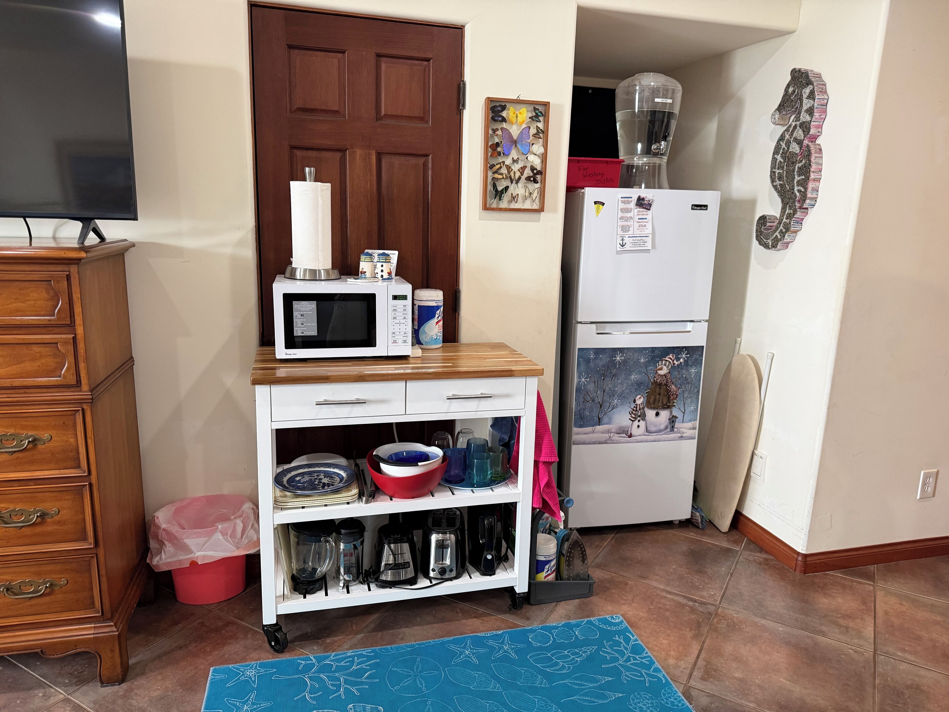 A compact kitchen with a microwave, refrigerator, and a small cabinet with dishes.