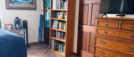 A bedroom with a bed, a bookshelf, a dresser, a television, and a painting on the wall.