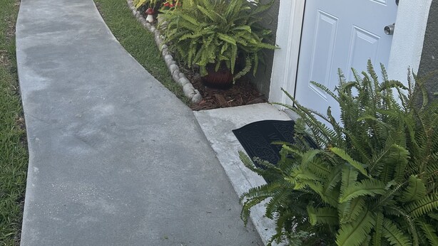 Uma casa com caminho de concreto que leva à porta da frente, decorada com uma grinalda floral.