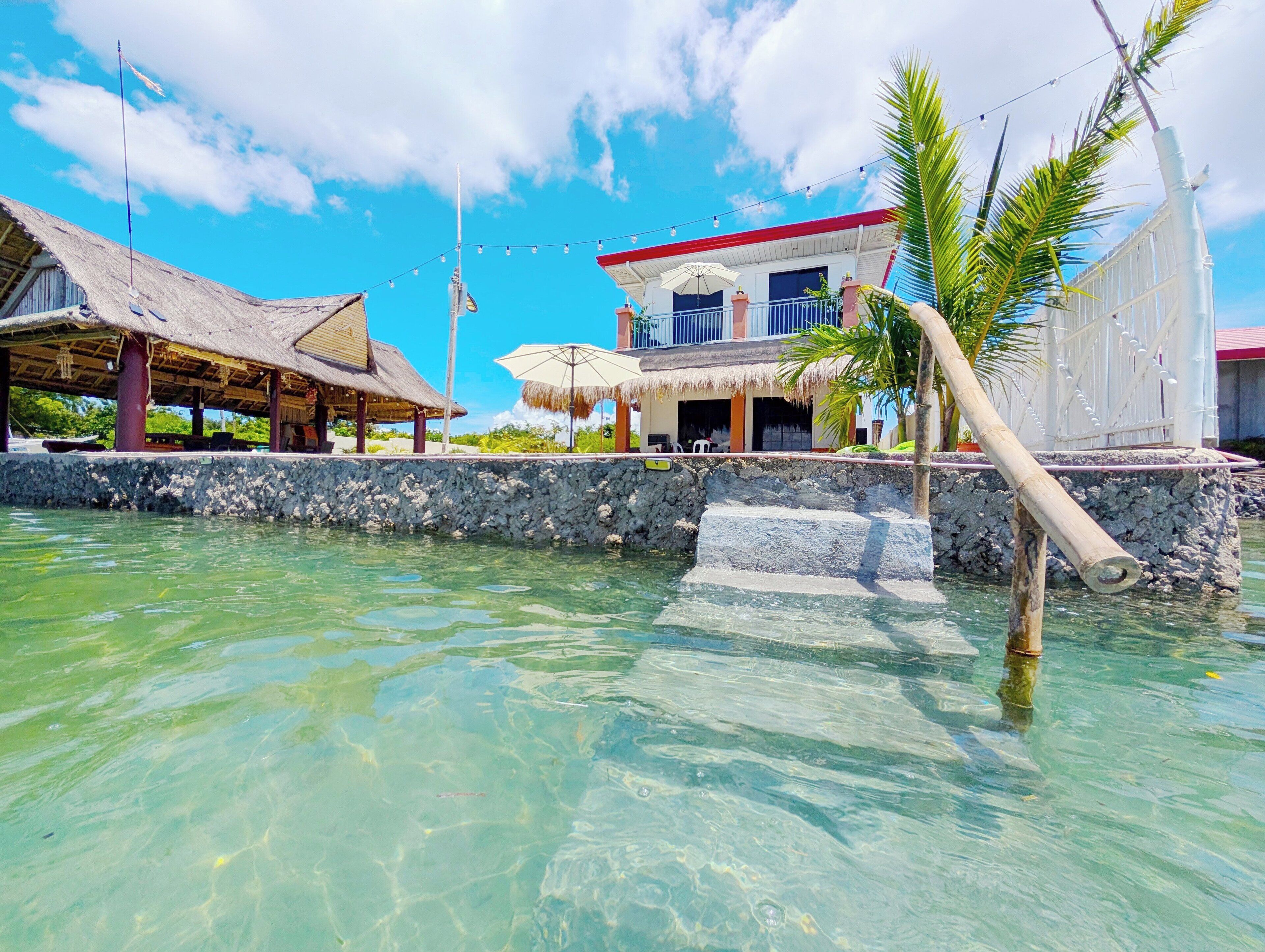 A beachfront property with a thatched-roof structure, a white building with a red roof, and a clear view of the ocean.
