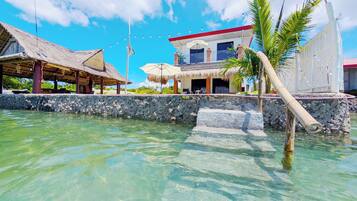 A beachfront property with a thatched-roof structure, a white building with a red roof, and a clear view of the ocean.