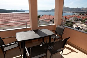 A balcony with a table and chairs, a view of a body of water, and buildings in the distance. - Charming 2-Bed Apartment in Okrug Gornji (Okrug Gornji)