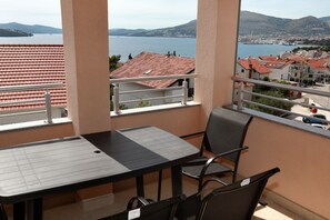 A balcony with a table and chairs, overlooking a body of water and a town. - Charming 2-Bed Apartment in Okrug Gornji (Okrug Gornji)