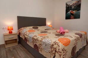 A neatly made bed with a floral bedspread, two bedside lamps, a wooden nightstand, and a painting on the wall. - Charming 2-Bed Apartment in Okrug Gornji (Okrug Gornji)