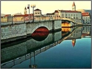 A stone bridge with a central arch over a calm body of water, reflecting the surrounding buildings and a tower. - Charming 2-Bed Apartment in Okrug Gornji (Okrug Gornji)