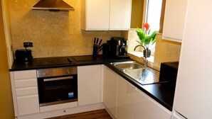 A compact kitchen with white cabinets, a built-in oven, a coffee machine, and a sink.