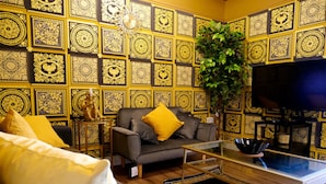 A living room with a sofa, a coffee table, and a television. The walls are decorated with intricate patterns.