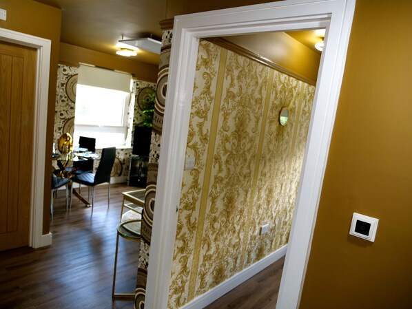 A room with a patterned wallpaper, a dining area with chairs and a table, and a window with natural light.