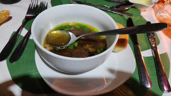 Un plato de sopa en un plato blanco, con una cuchara, sobre un tapete verde.