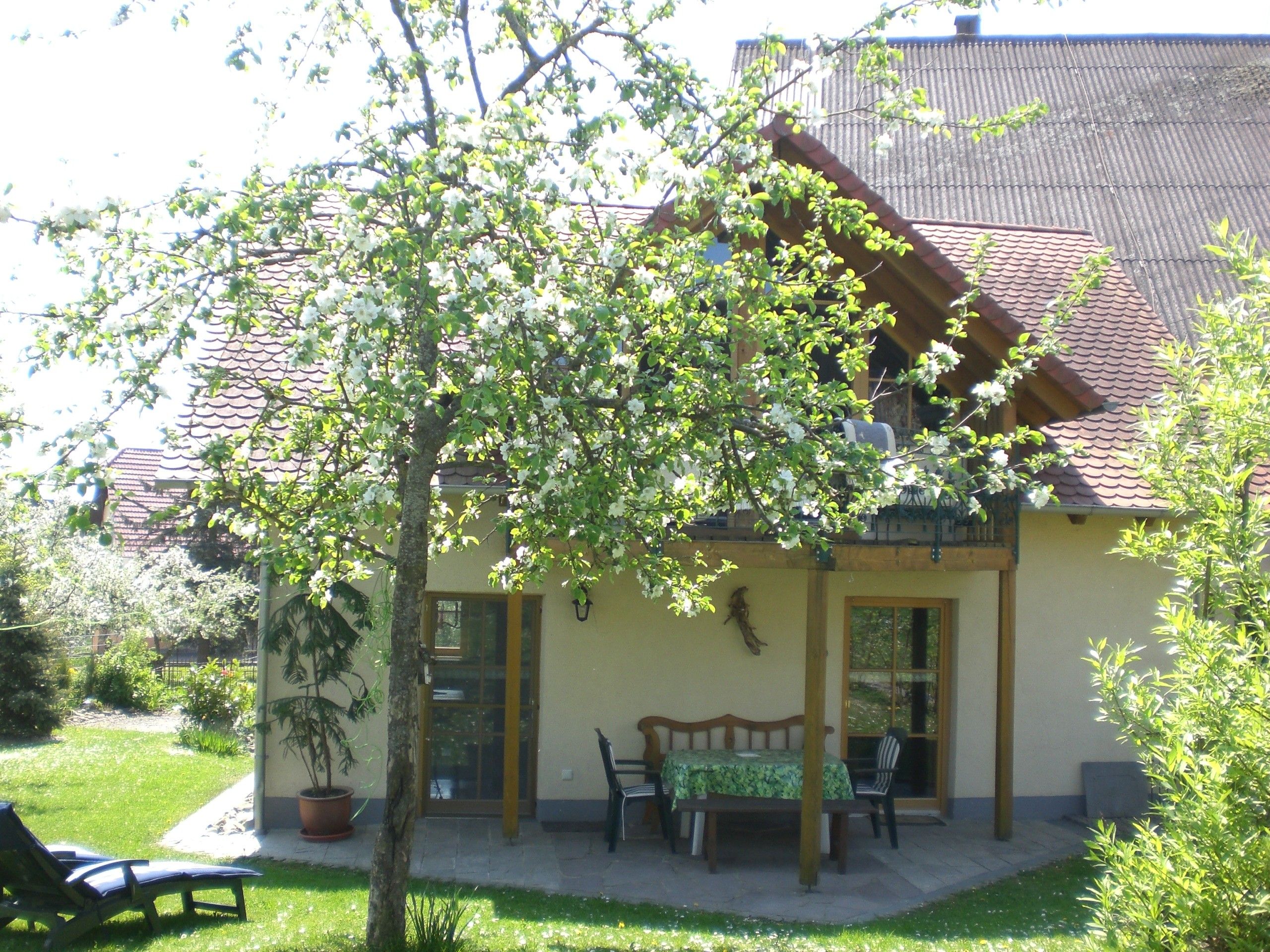 Een huis met een pannendak, een tuin met een bankje en een tafel met stoelen.