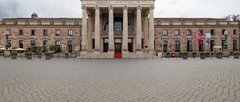 A large building with a central entrance flanked by columns, a red staircase, and a paved courtyard.