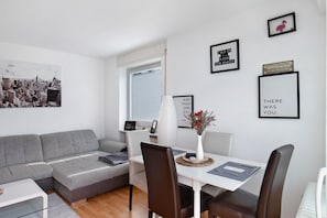 Un salon moderne avec un canapé gris, une table à manger et des chaises, ainsi qu’un tableau représentant un paysage urbain.