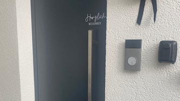 Une porte noire avec une poignée verticale et une pancarte indiquant « Bienvenue » au-dessus.