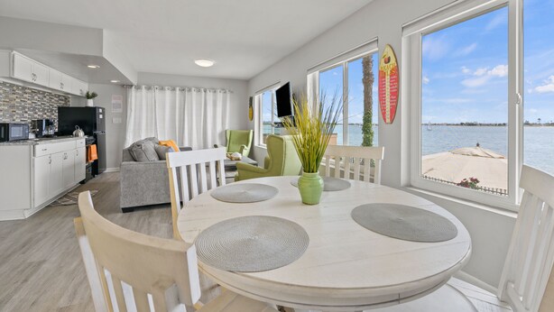 Una cucina moderna con mobili bianchi, un'area pranzo con tavolo e sedie rotonde, e vista sulla spiaggia attraverso ampie finestre.