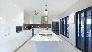 A modern kitchen with white cabinets, a central island, and a large window. - ZENHOUSE - 5BR Family with Private Pool (Johnston)
