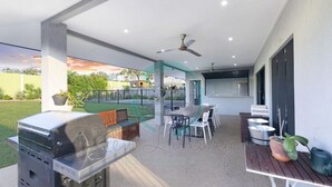 An outdoor patio with a grill, dining table, chairs, and a ceiling fan. - ZENHOUSE - 5BR Family with Private Pool (Johnston)