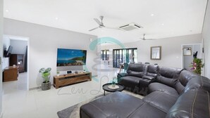 A modern living room with a large sectional sofa, a flat-screen TV, and a ceiling fan. - ZENHOUSE - 5BR Family with Private Pool (Johnston)