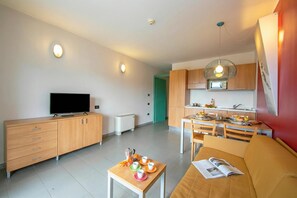 Un salon moderne comprenant un canapé, une table basse avec un magazine, un téléviseur et un coin repas avec une table et des chaises.