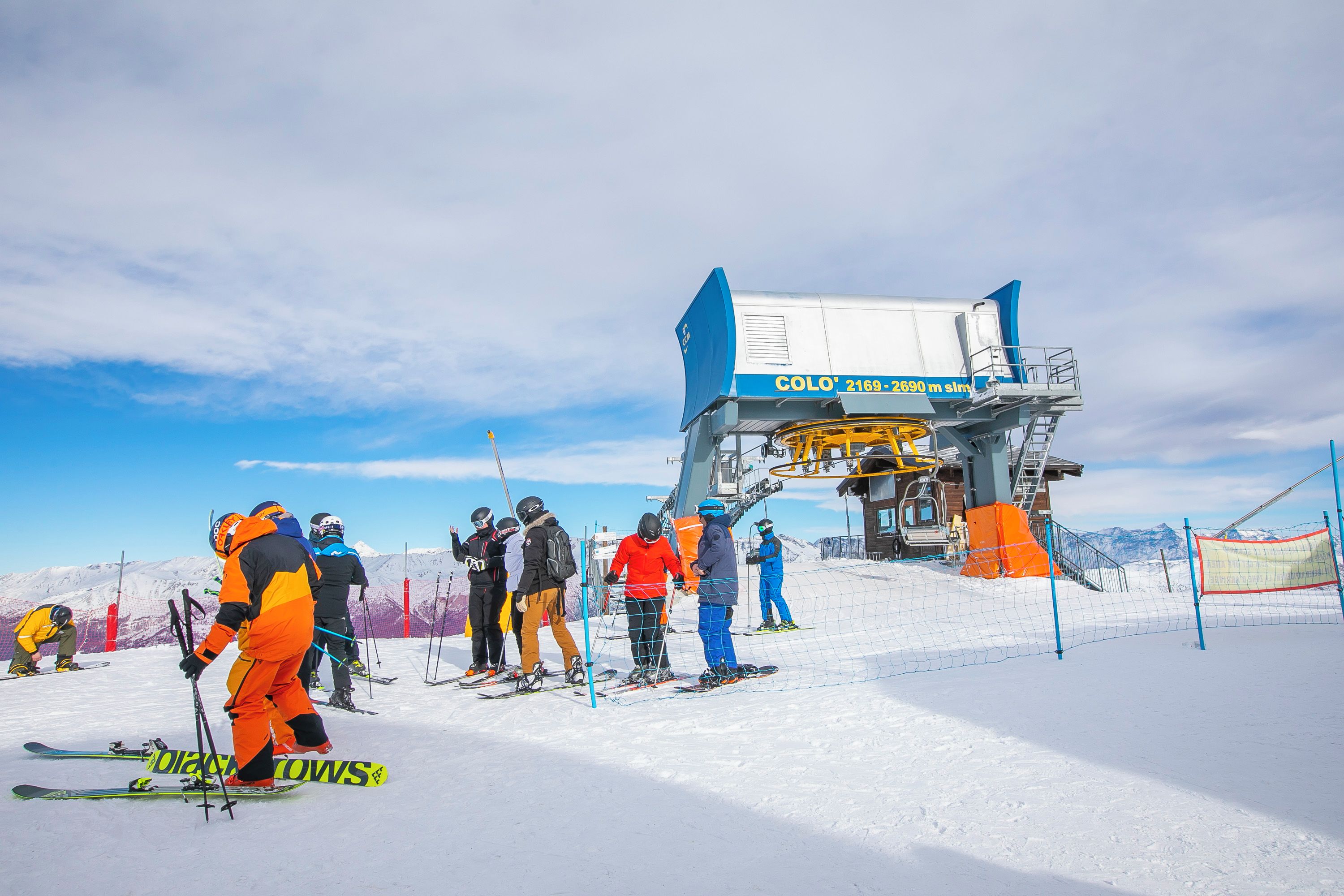 Eine Sesselbahn mit blauer und weißer Konstruktion, umgeben von Skifahrern an einem verschneiten Hang.