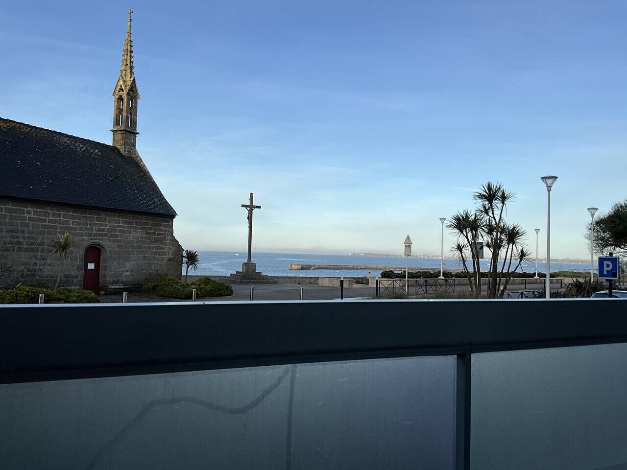 A coastal view with a church, a cross monument, and a lighthouse in the distance.