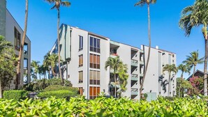 Un hotel moderno de varios pisos con balcones, rodeado de exuberante vegetación y palmeras.