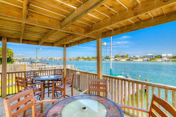 Relax in a covered outdoor seating area with a deck overlooking a marina and distant buildings.