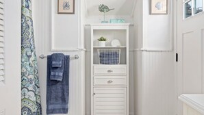 A bathroom with a shower curtain, a towel rack, a small shelf with decorative items, and a white cabinet with drawers.
