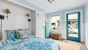 A bedroom with a bed, a dresser, a mirror, a door, and a window.