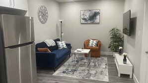 A modern living room with a blue sofa, a brown armchair, a white coffee table, a clock, and a painting on the wall. - Unique and Spacious 1BR Basement near Anthony Henday.  (Edmonton)
