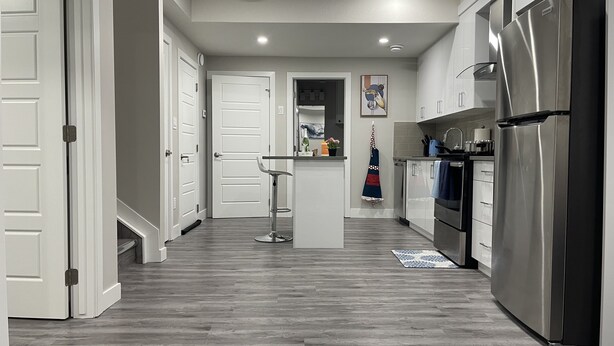 A modern kitchen with a stainless steel refrigerator, white cabinetry, and a wooden floor. - Unique and Spacious 1BR Basement near Anthony Henday.  (Edmonton)