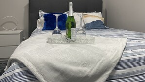 A neatly made bed with a white and blue patterned bedspread, a green bottle, and two clear wine glasses on a decorative tray. - Unique and Spacious 1BR Basement near Anthony Henday.  (Edmonton)