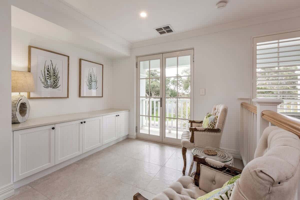 Una habitación amplia con un gran ventanal corredero que da a un balcón, un sillón mullido, una pequeña mesa redonda y un armario con una lámpara.