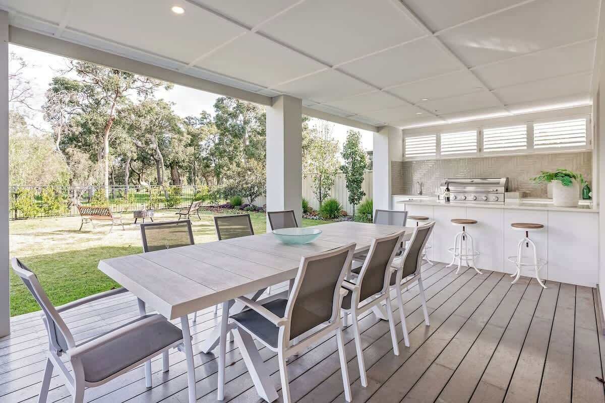 An outdoor patio with a dining table and chairs, a grill, and a view of the surrounding garden.