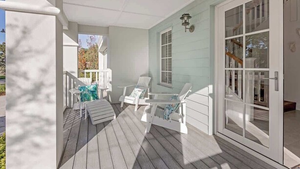 A covered porch with white chairs and a table, a sliding glass door, and a light blue exterior wall. - Hamptons By The Green—Grand Golfside Retreat (DUNSBOROUGH)