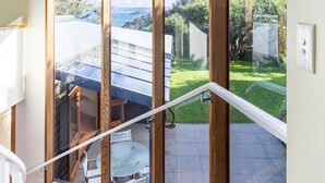A staircase leading to a balcony with large windows, a view of a garden, and a white building in the background. - Sea views from holiday house (Lower Hutt)
