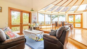 A spacious living room with a large glass ceiling, leather sofas, a coffee table, and a dining area with chairs. - Sea views from holiday house (Lower Hutt)