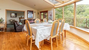 A dining area with a table set for four, wooden chairs, and a large window with a view of greenery. - Sea views from holiday house (Lower Hutt)