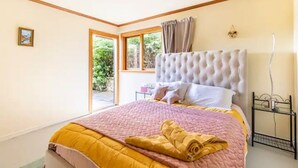 A bedroom with a large bed, a window with a view of greenery, and a bedside table with a lamp. - Sea views from holiday house (Lower Hutt)