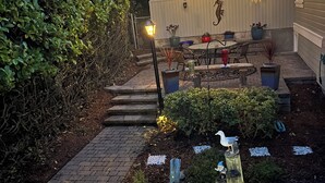 A garden with a patio, potted plants, and a bird sculpture. - Make Victoria View your home base while exploring PNW! Garage to store your toys (Port Angeles)