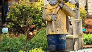 A wooden sculpture of a figure holding a bird, surrounded by potted plants and a sign that reads "THE LIL". - Make Victoria View your home base while exploring PNW! Garage to store your toys (Port Angeles)