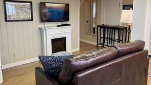 A living room with a fireplace, a television, a sofa, and a map on the wall. - Make Victoria View your home base while exploring PNW! Garage to store your toys (Port Angeles)