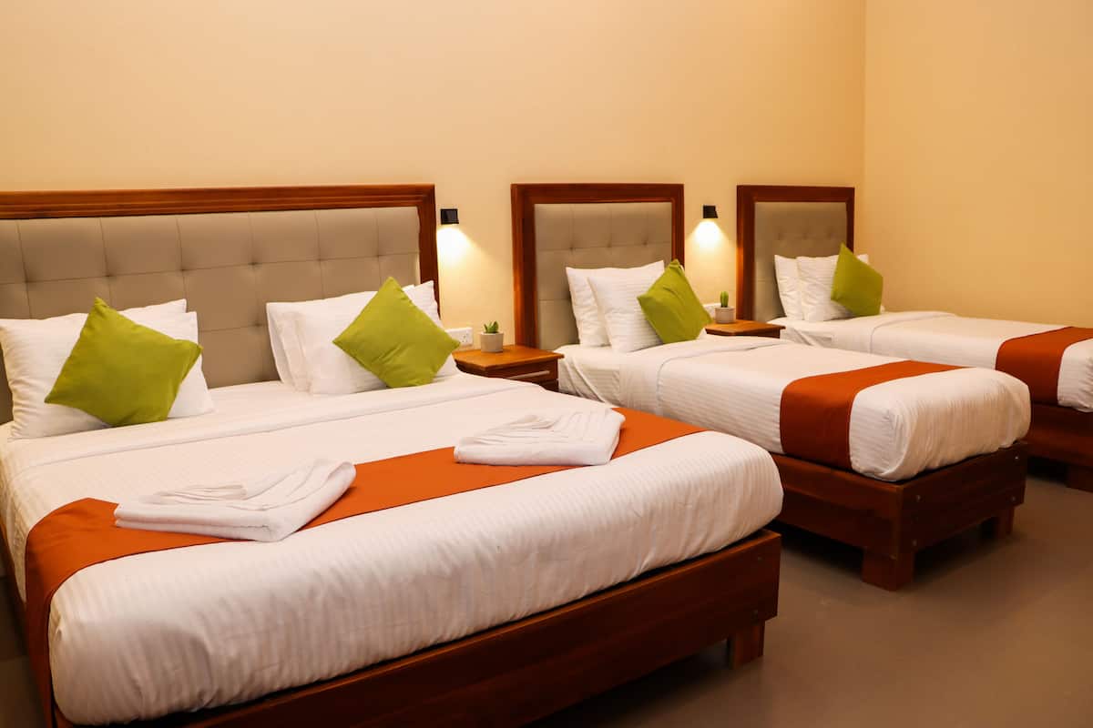 A hotel room with three beds, each with white bedding and green pillows.