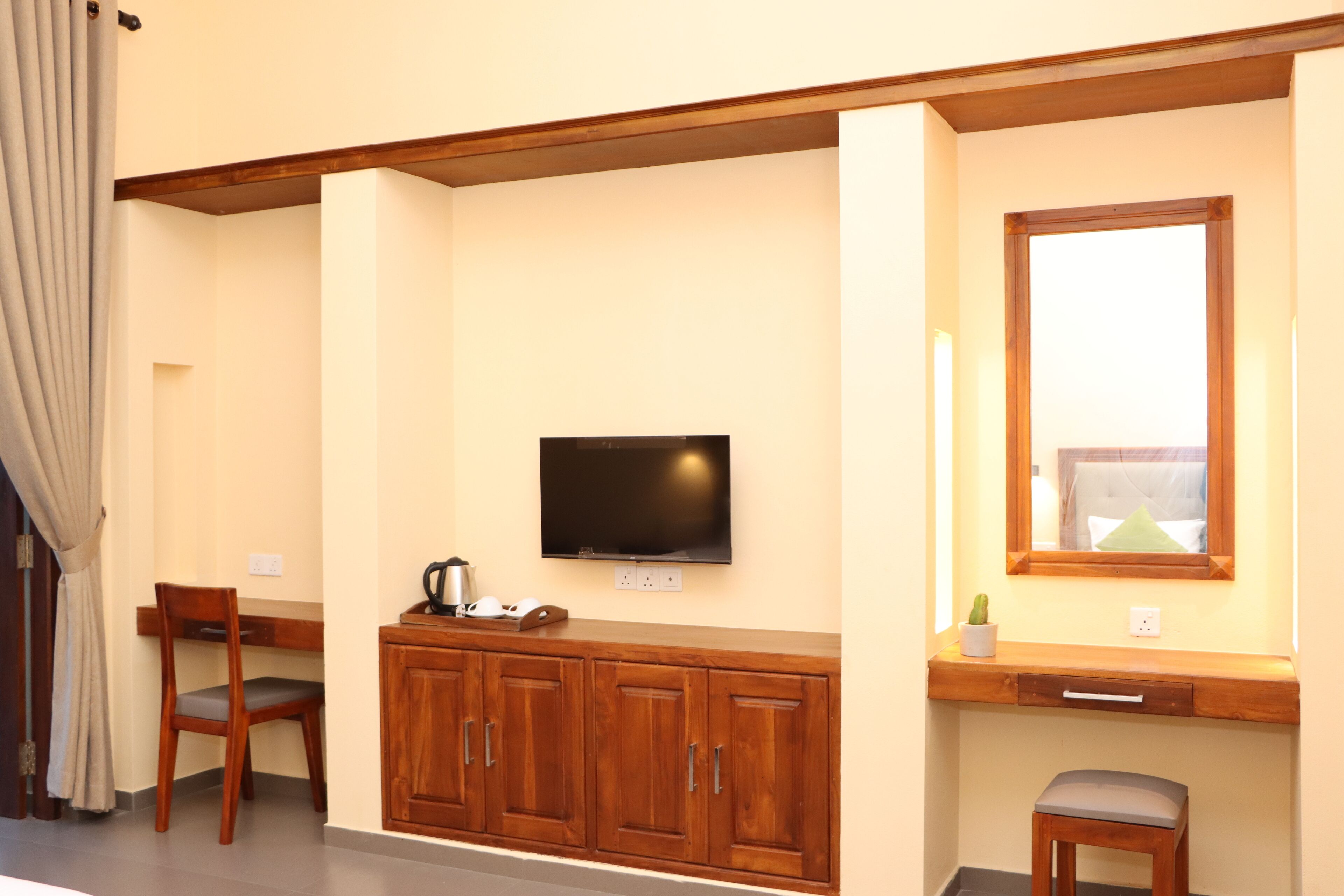 Una habitación con un armario de madera, un televisor montado en la pared, un taburete pequeño y una ventana con vistas.
