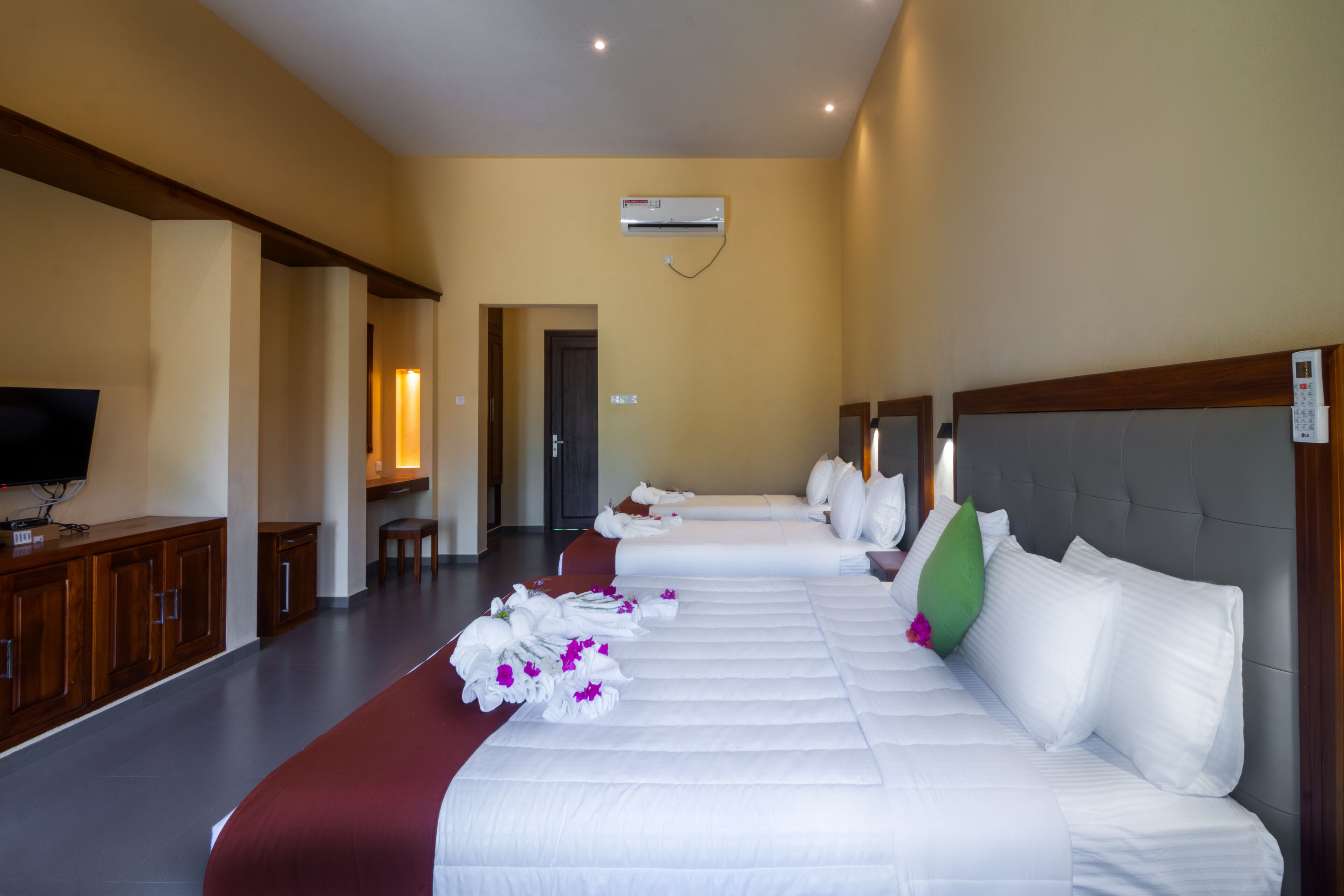 Quarto de hotel com três camas, uma televisão e um aparelho de ar condicionado.