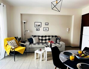 Una sala de estar con un sofá, una mesa de comedor y una mesa de centro. Hay cuadros en la pared.