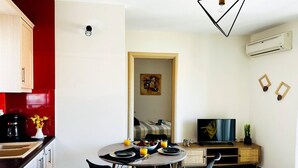 A modern kitchen with a dining area, a TV, and a red accent wall. - Cozy Snuggle- 2min To Beach, 6min Walk To Old Town (Chania)