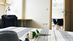 A bedroom with a bed, a desk, a chair, and a door leading to a dining area. - Cozy Snuggle- 2min To Beach, 6min Walk To Old Town (Chania)