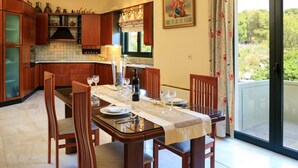 Un comedor con una mesa lista para cuatro personas, armarios de madera, una ventana con cortinas y una puerta que da a un espacio exterior.