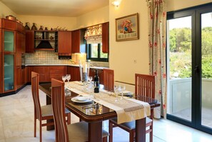 Un coin repas avec une table dressée pour quatre personnes, des meubles en bois, une fenêtre avec des rideaux et une porte donnant sur un espace extérieur.